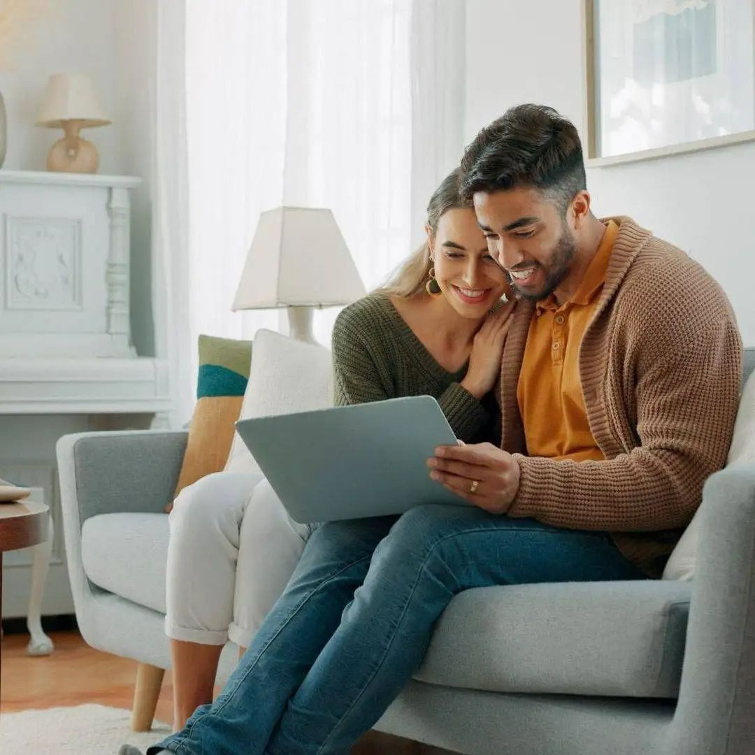 A man and a woman are sitting on a couch looking at a laptop.