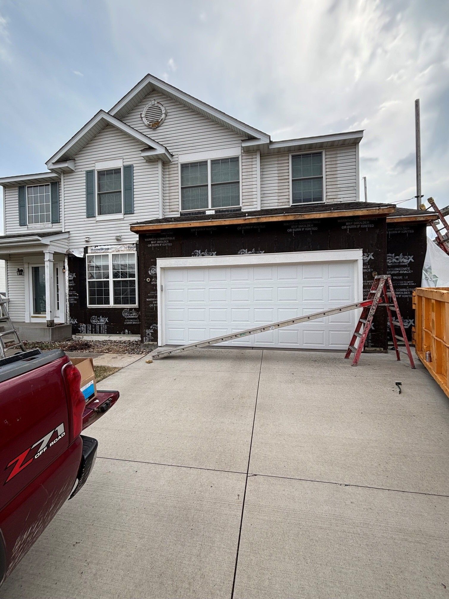 House with attached garage under construction, driveway in front, red ladder and parked truck visible