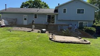 Backyard with a small house, patio doors, and a person standing near a rock garden.