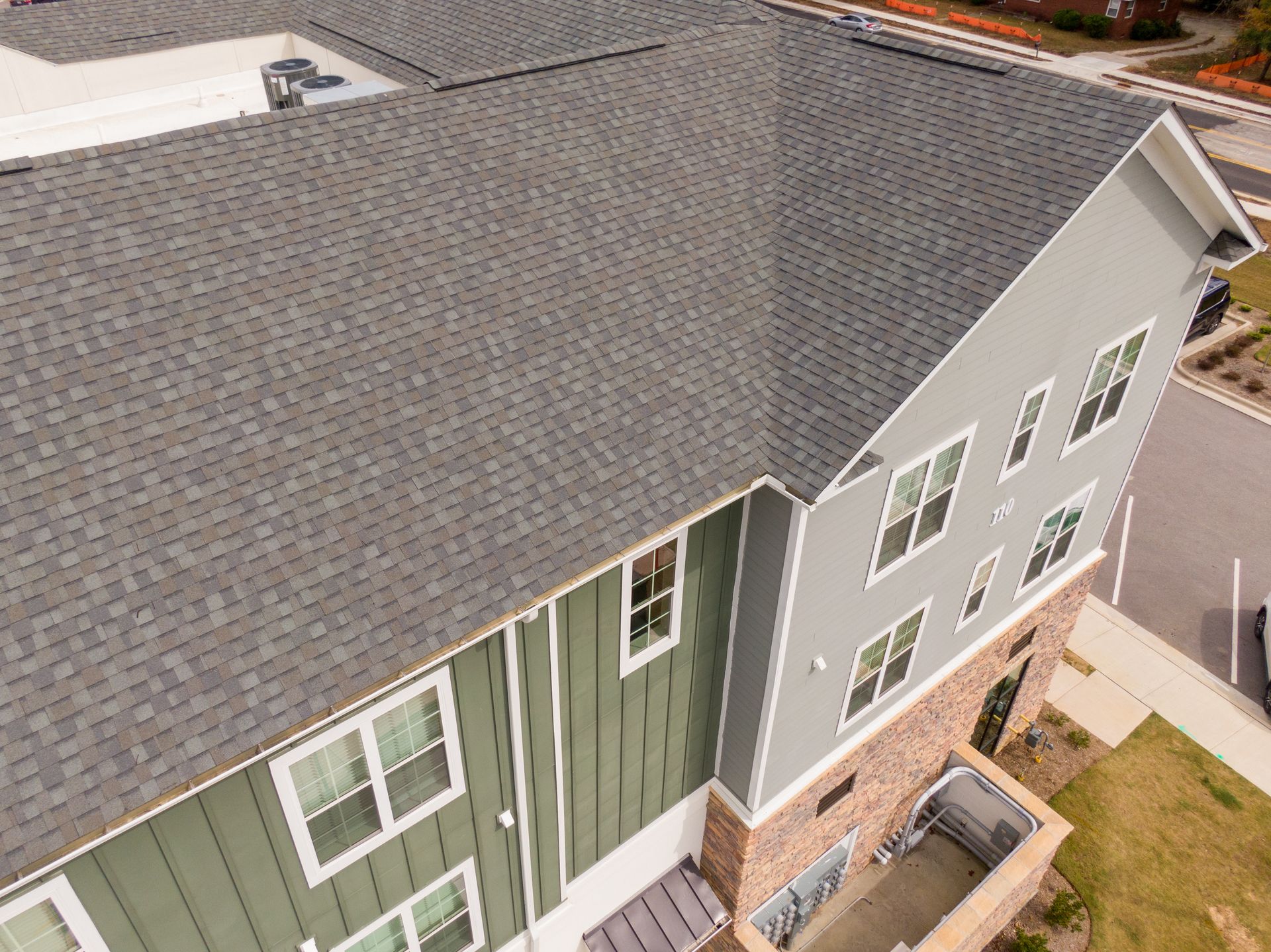 Overhead view of a building with a dark gray shingle roof and green and gray siding.