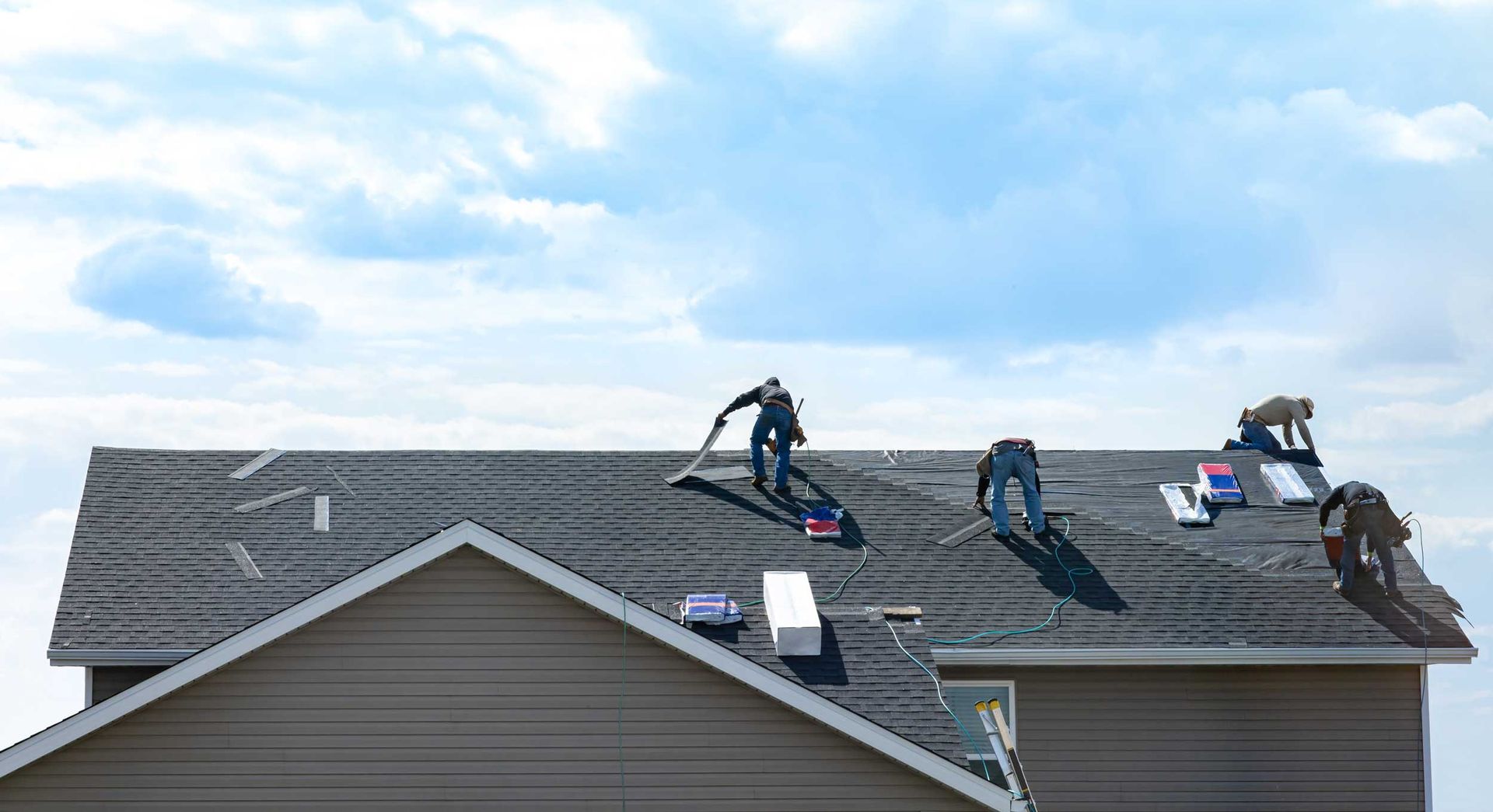 Workers installing shingles on a house roof using tools and materials
