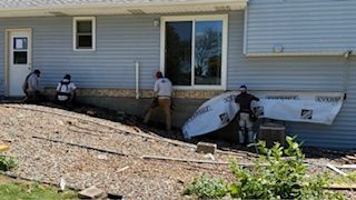 Workers inspect damage to a house’s exterior wall and siding near a sliding glass door.