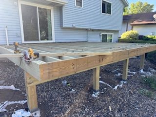 New wooden deck frame under construction beside a gray house, with support posts and exposed joists.