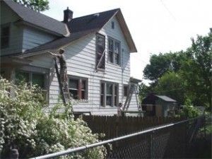 A man is standing on a ladder on the side of a house.