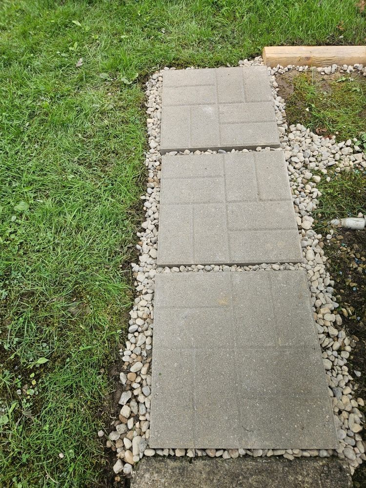 A stone pathway with gray paving stones edged by small pebbles, next to green grass.