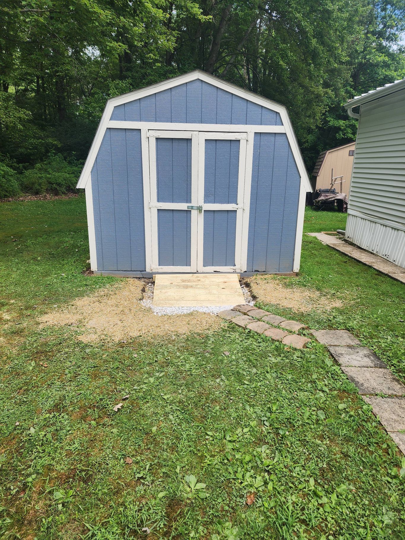Blue shed with white trim and double doors, in a yard with a stone path.