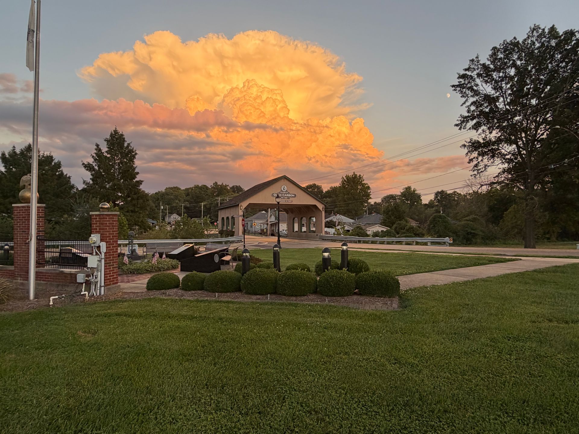 Sunset over park with large pavilion, clouds lit orange, and green lawn.
