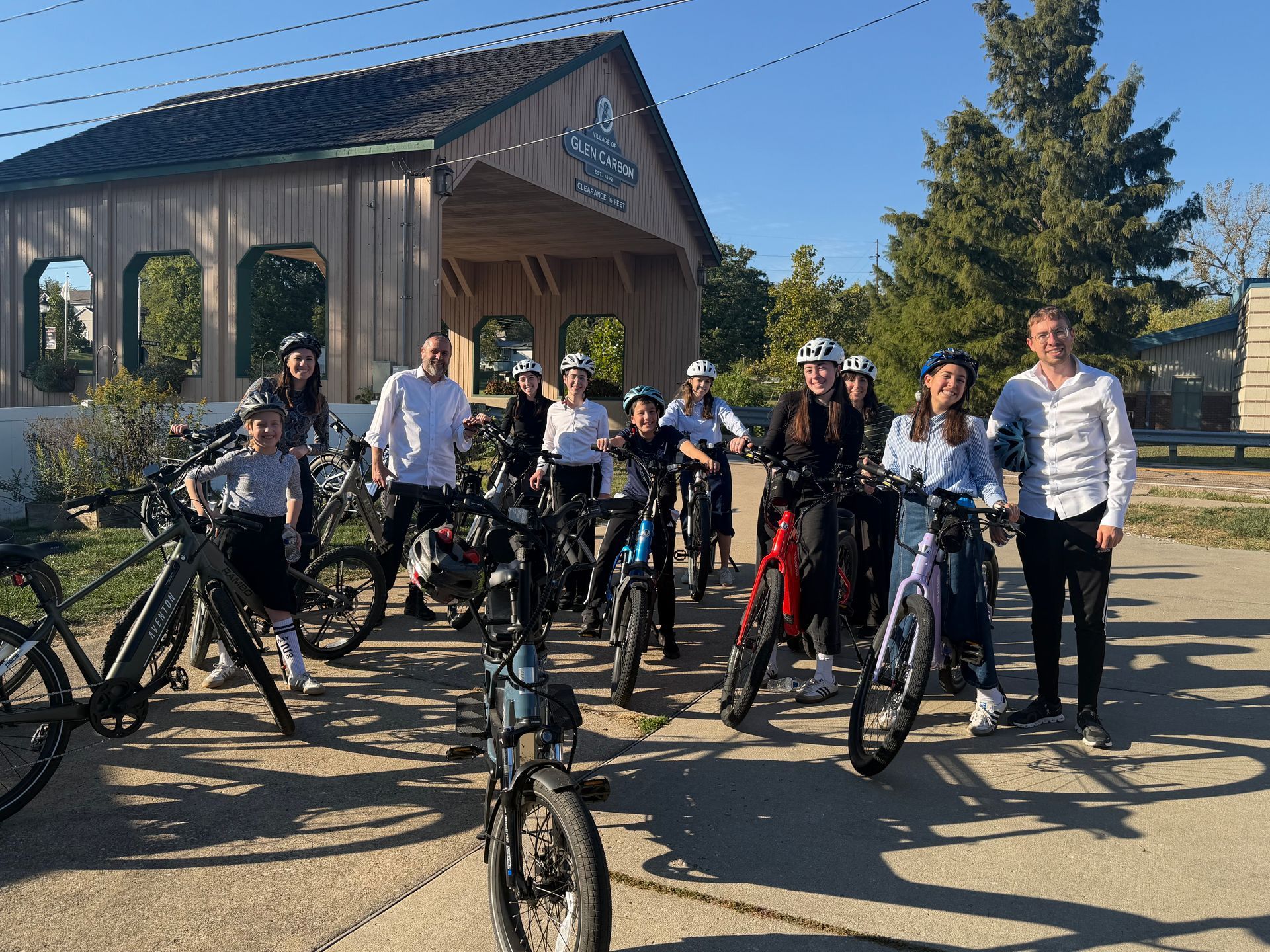 Group of people on bicycles in front of a wooden structure; sunny day.