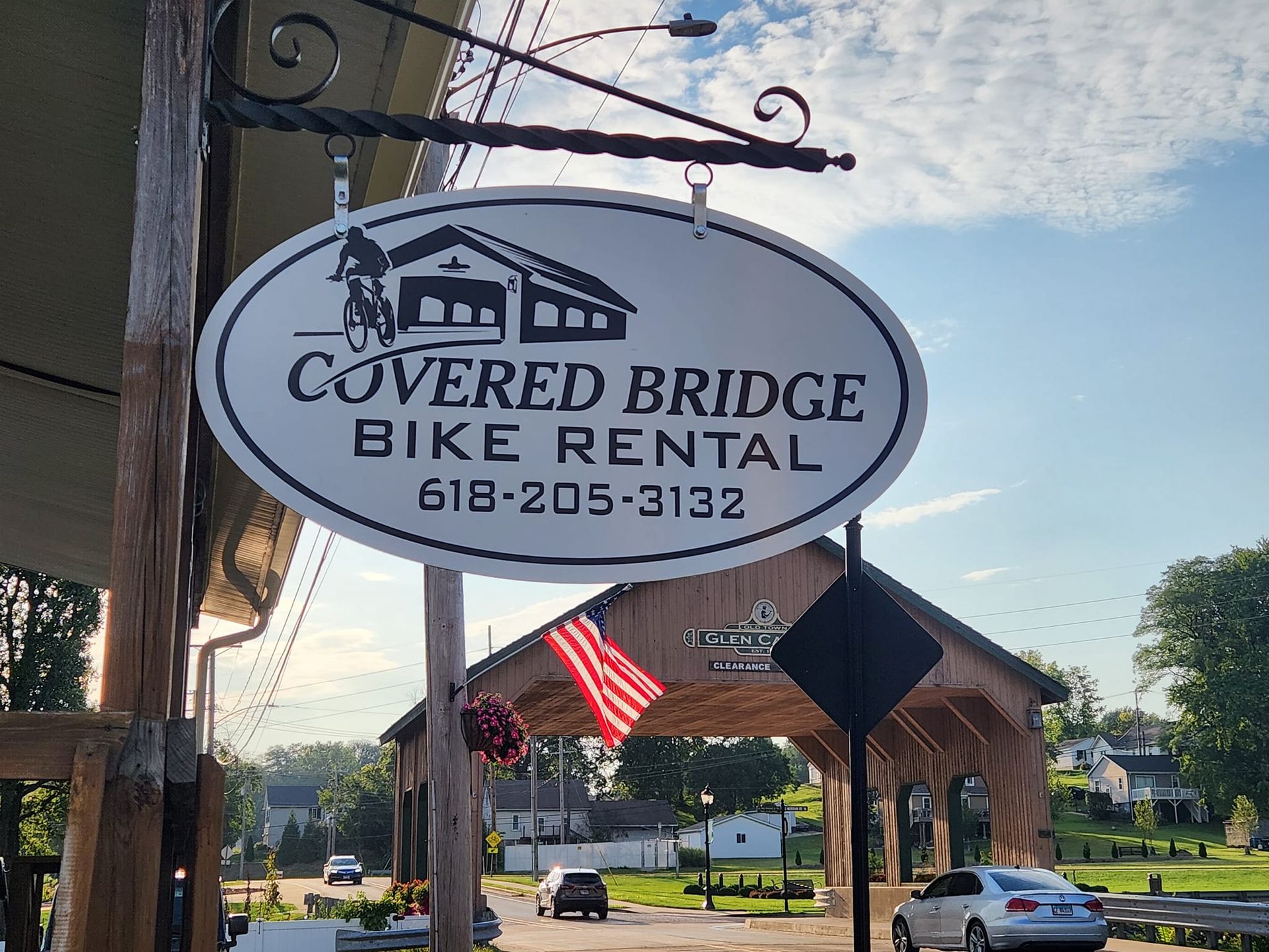 Sign for Covered Bridge Bike Rental, with a bridge in the background. Oval sign is white with black text and an image of a person biking.