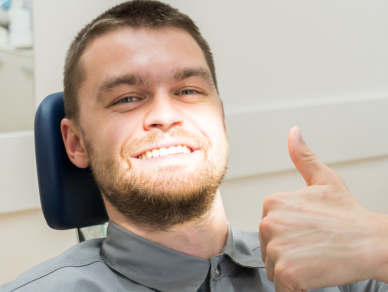 A man is sitting in a dental chair and giving a thumbs up.