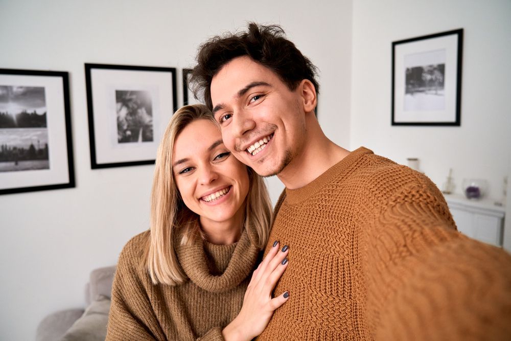 A man and a woman are taking a selfie together in a living room.