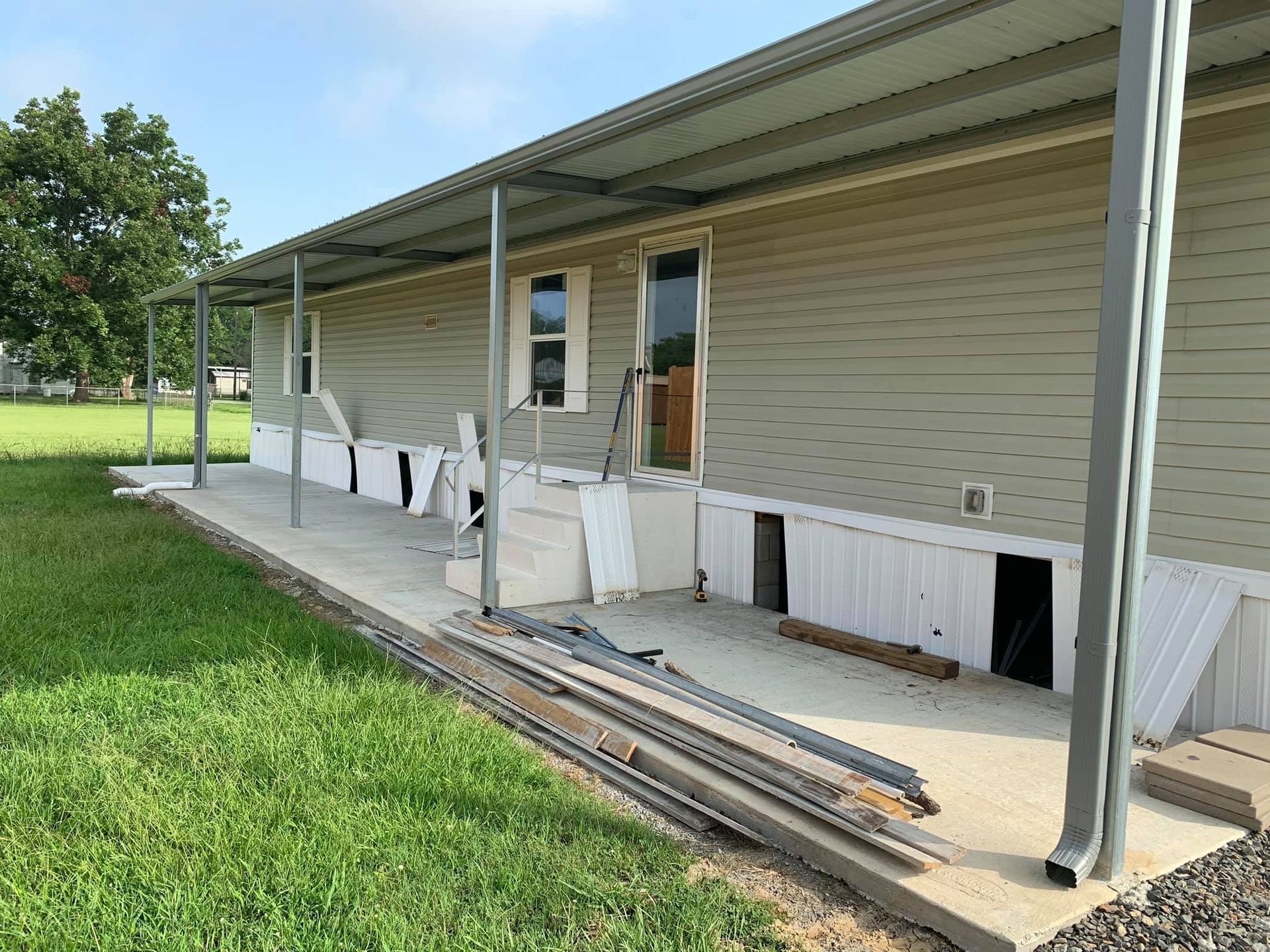 Mobile home with a concrete porch and metal awning under construction. Green siding and grass.