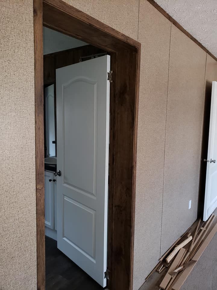 A white door with a wooden frame is open in a hallway.