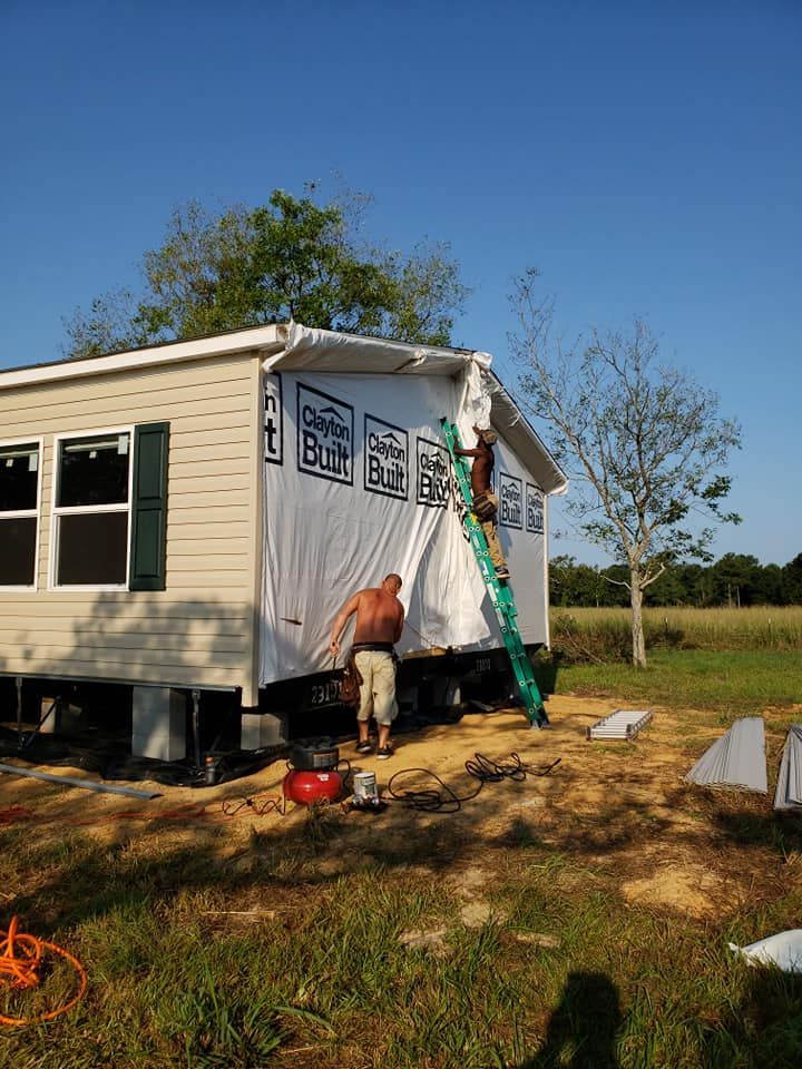 A man is standing on a ladder painting the side of a mobile home.