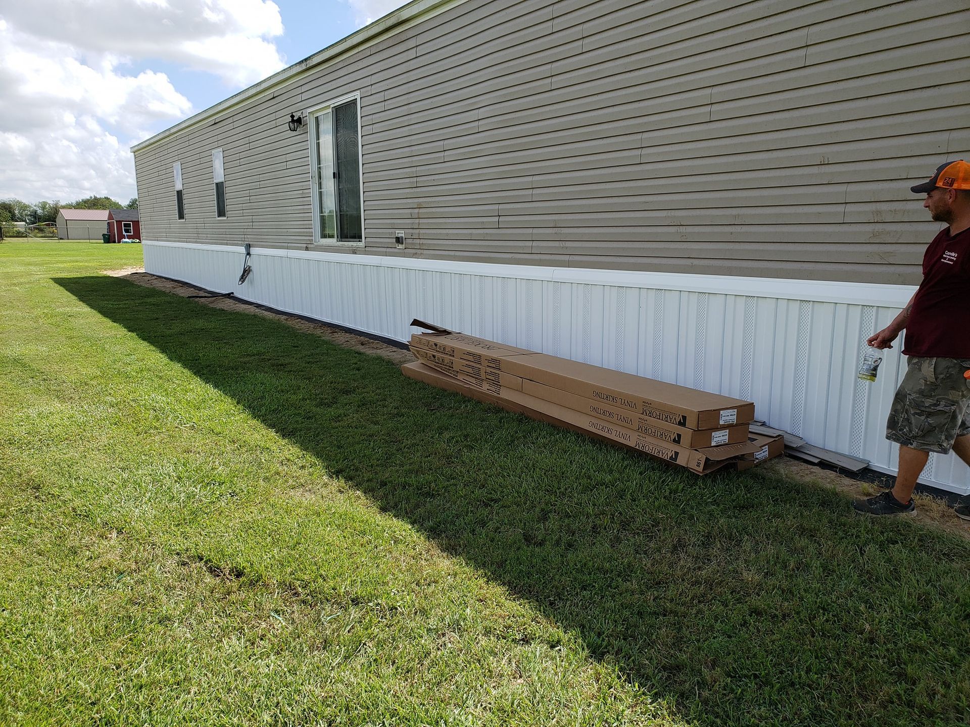 A man is standing in front of a mobile home with a white fence.
