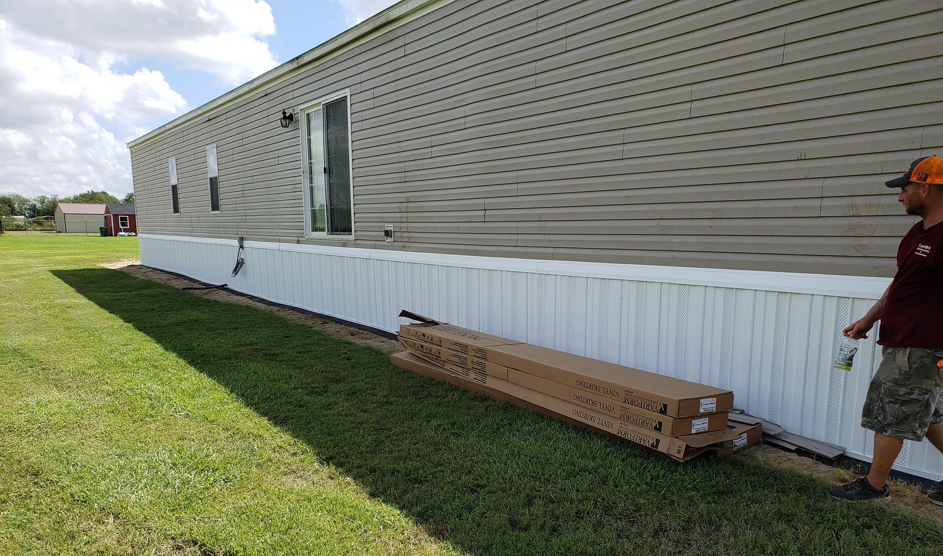 A man is painting a white fence in front of a mobile home.