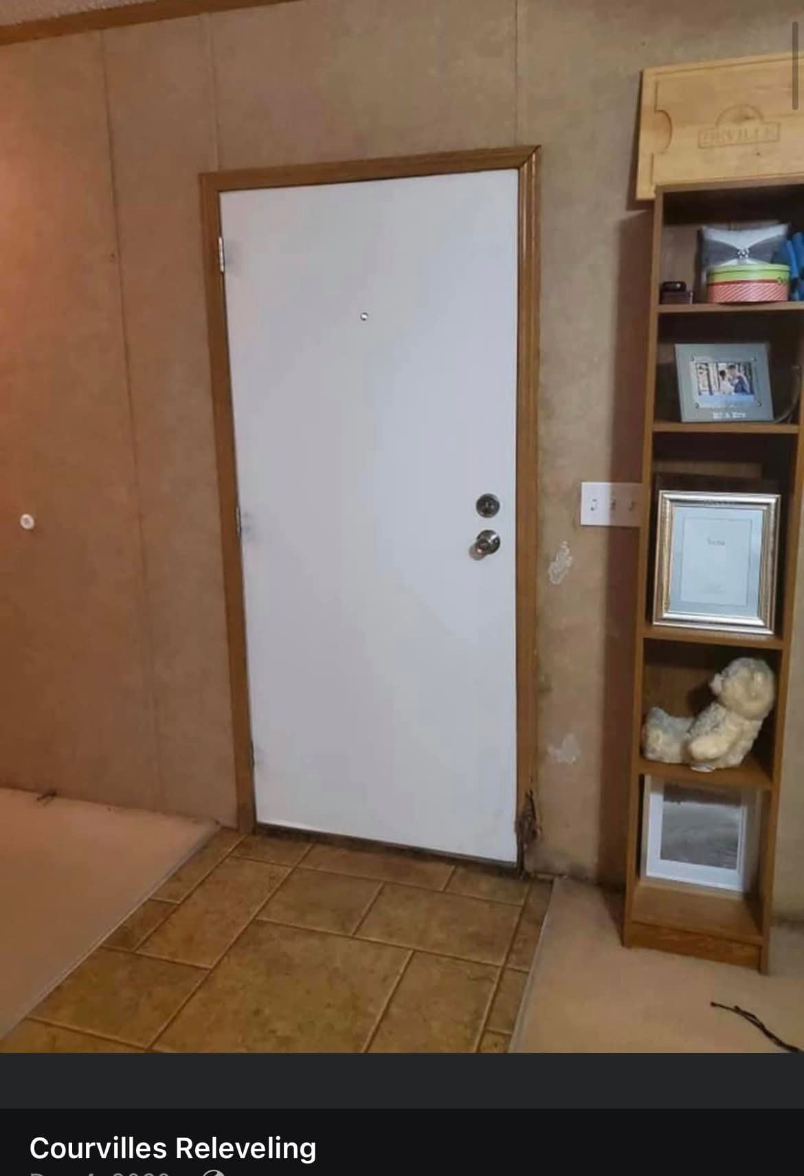 White door with dark wood trim and shelving unit. Entryway with tile floor and neutral walls.