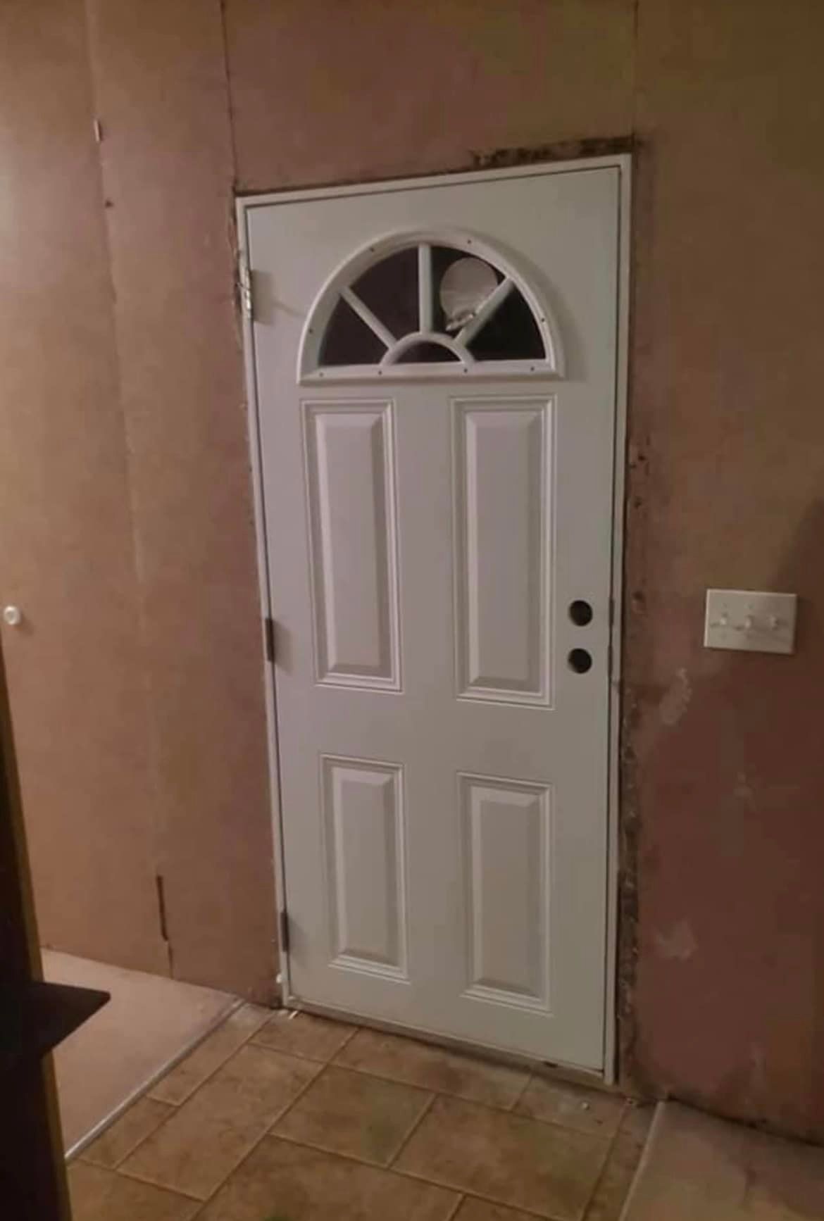 White door with arched window, set in a tan-colored wall.