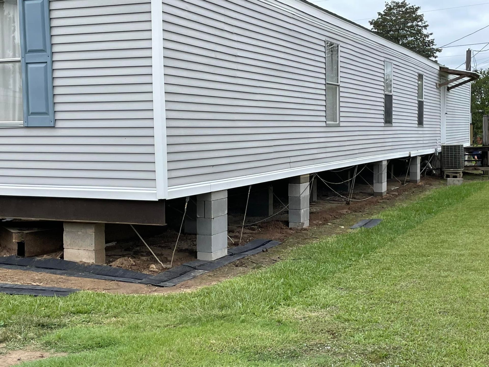 A mobile home is sitting on stilts in a grassy field.