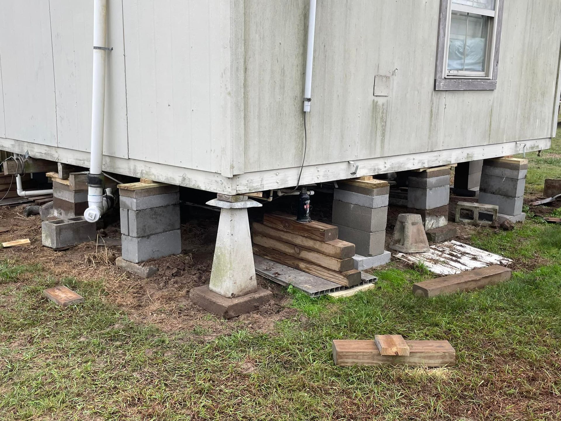 Mobile home elevated on cinder blocks and a concrete pedestal, outdoors.