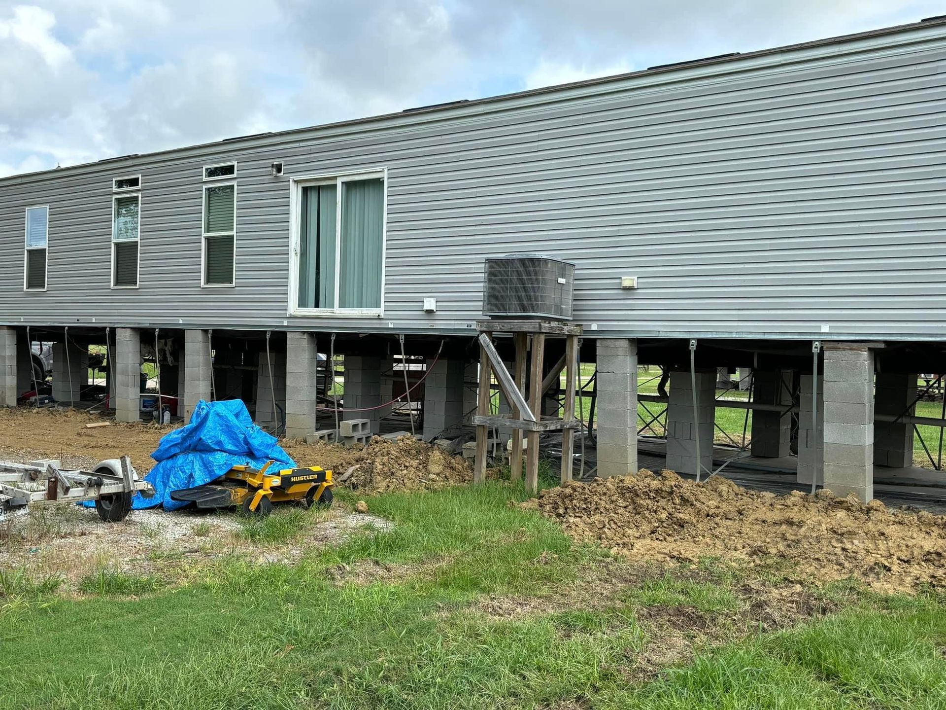 A mobile home is being built on stilts in a grassy field.