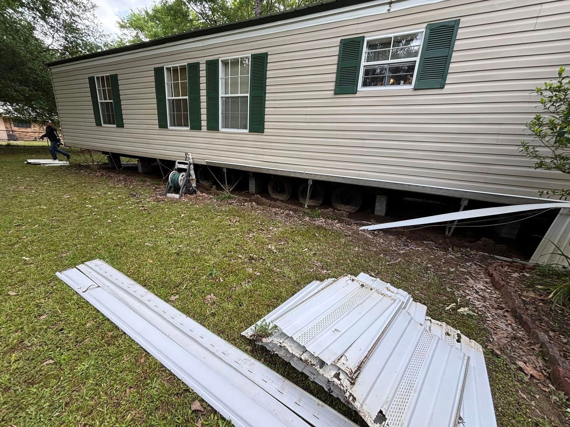 A mobile home with green shutters is sitting on top of a lush green field.