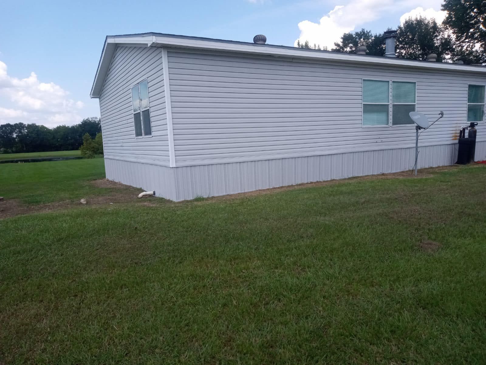 A white mobile home is sitting in the middle of a grassy field.