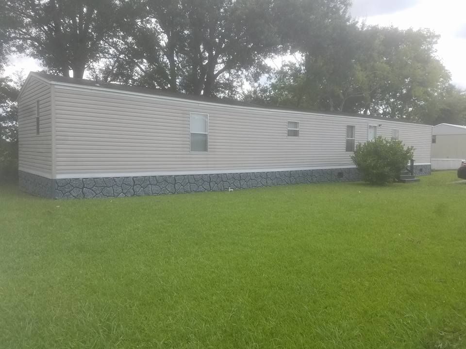 Mobile home with light siding, set on a stone foundation, in a grassy yard with trees.