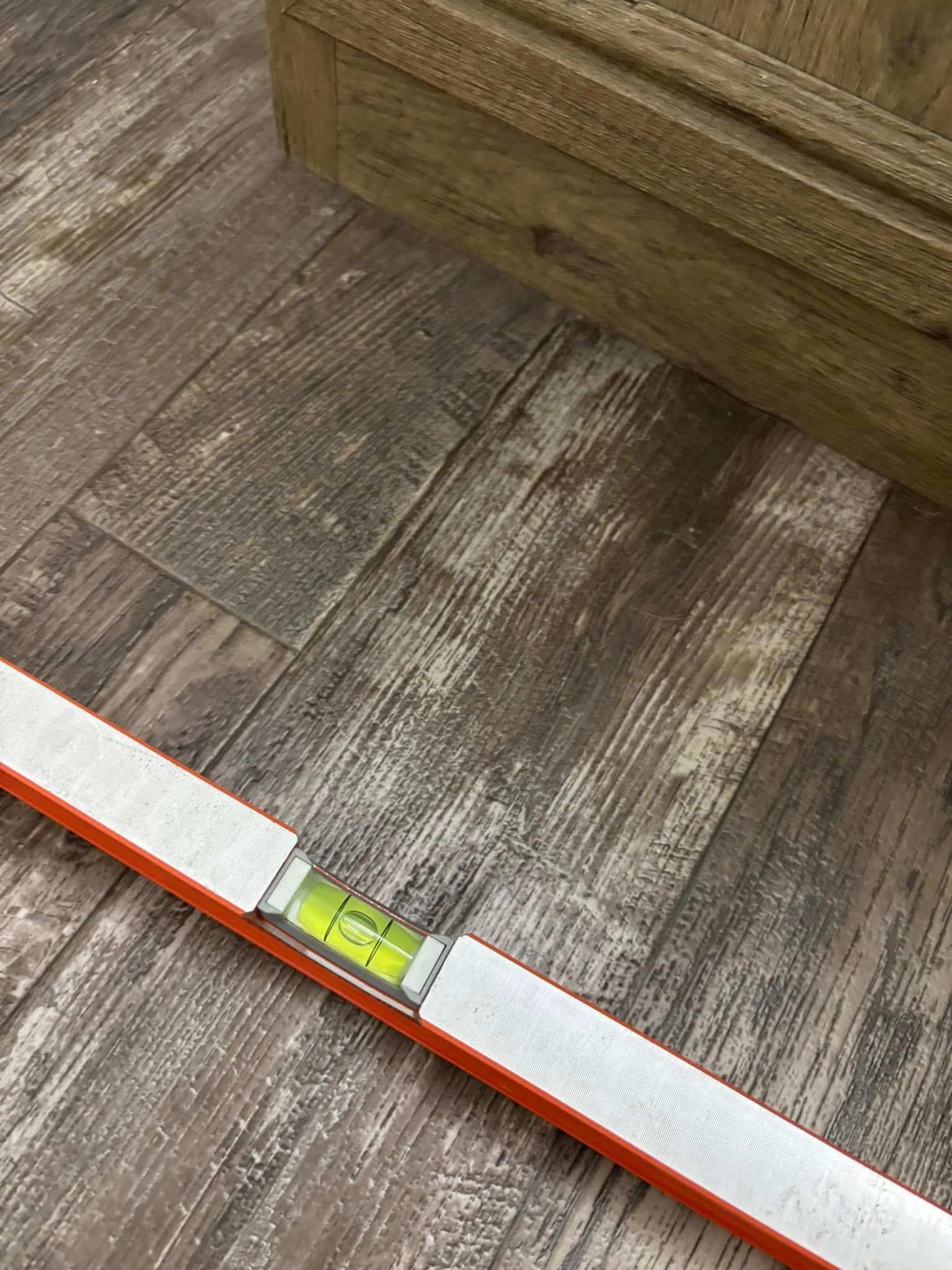 A level is sitting on a wooden floor next to a wooden box.