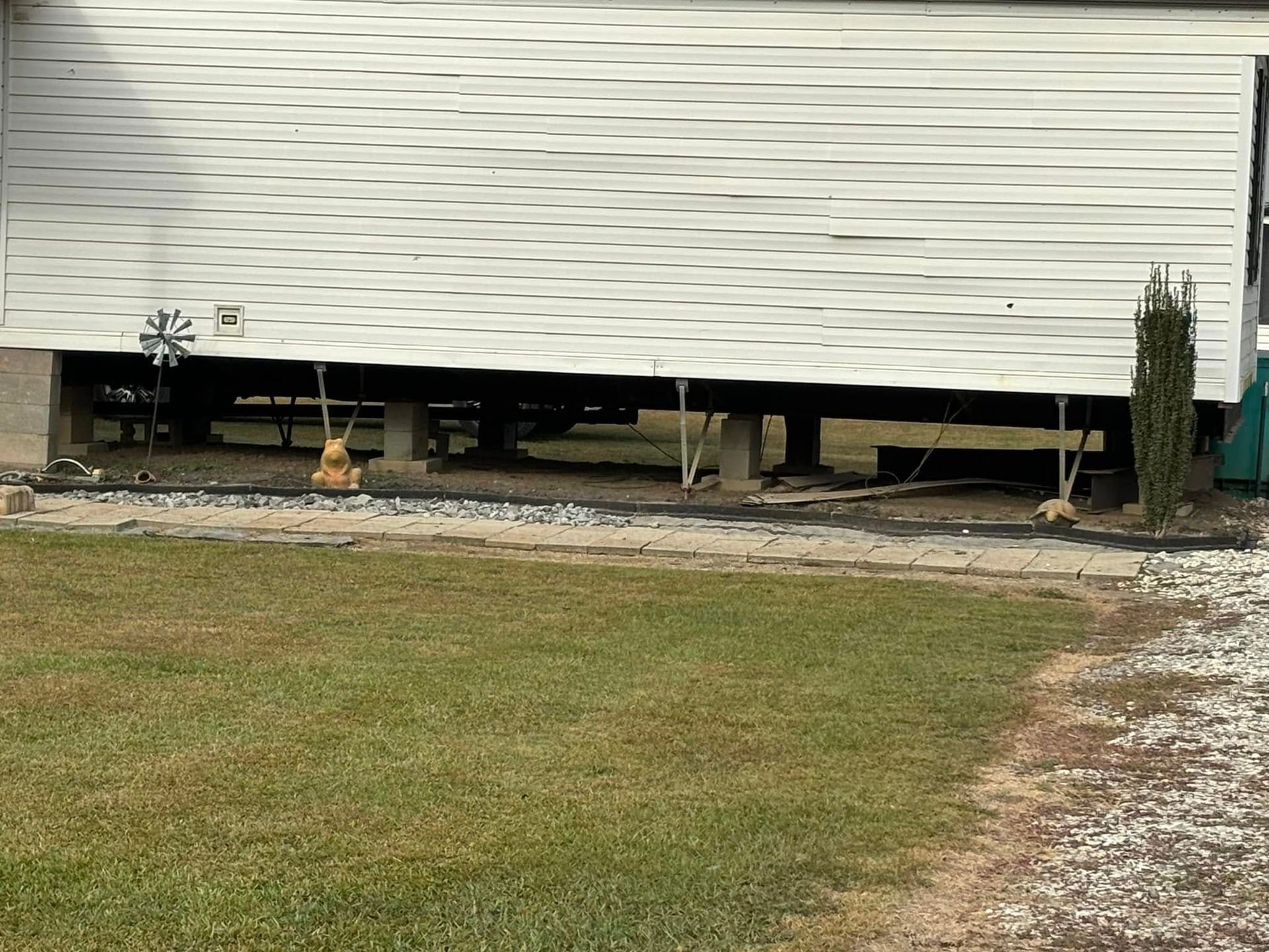 A white house with a broken garage door is sitting on top of a lush green field.