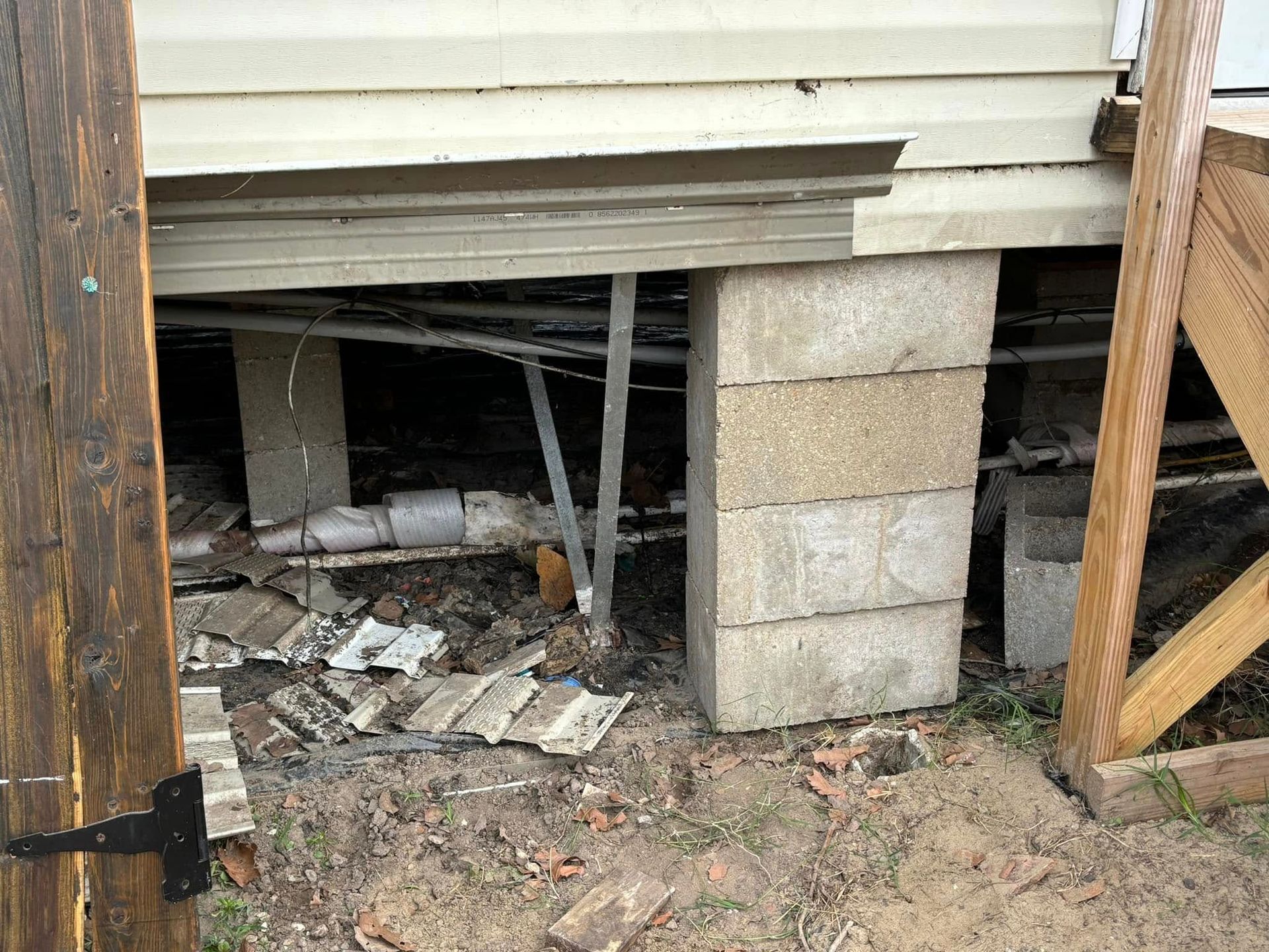 A concrete block is sitting under a house next to a wooden fence.