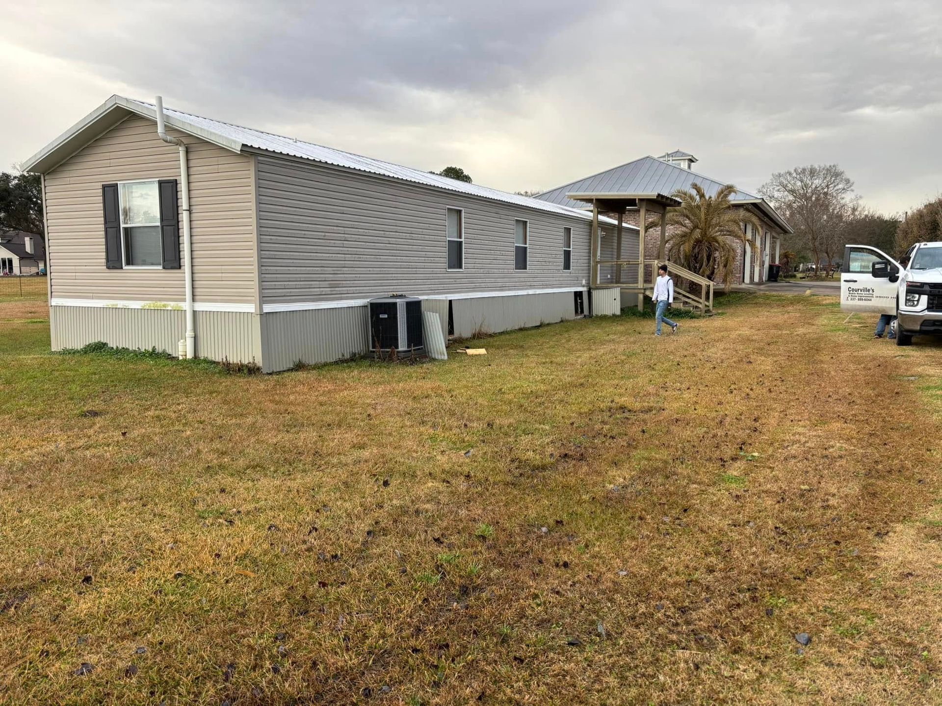 A man is standing in front of a mobile home in a field.