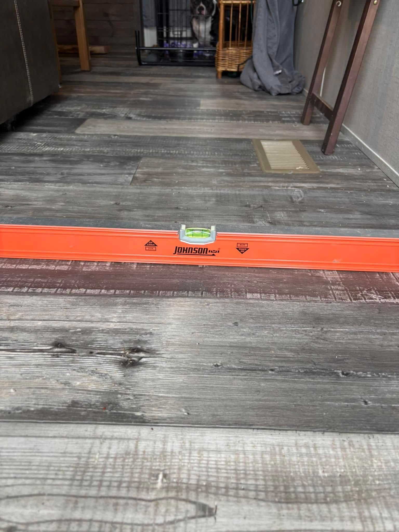 A wooden floor with a level on it and a dog in the background.