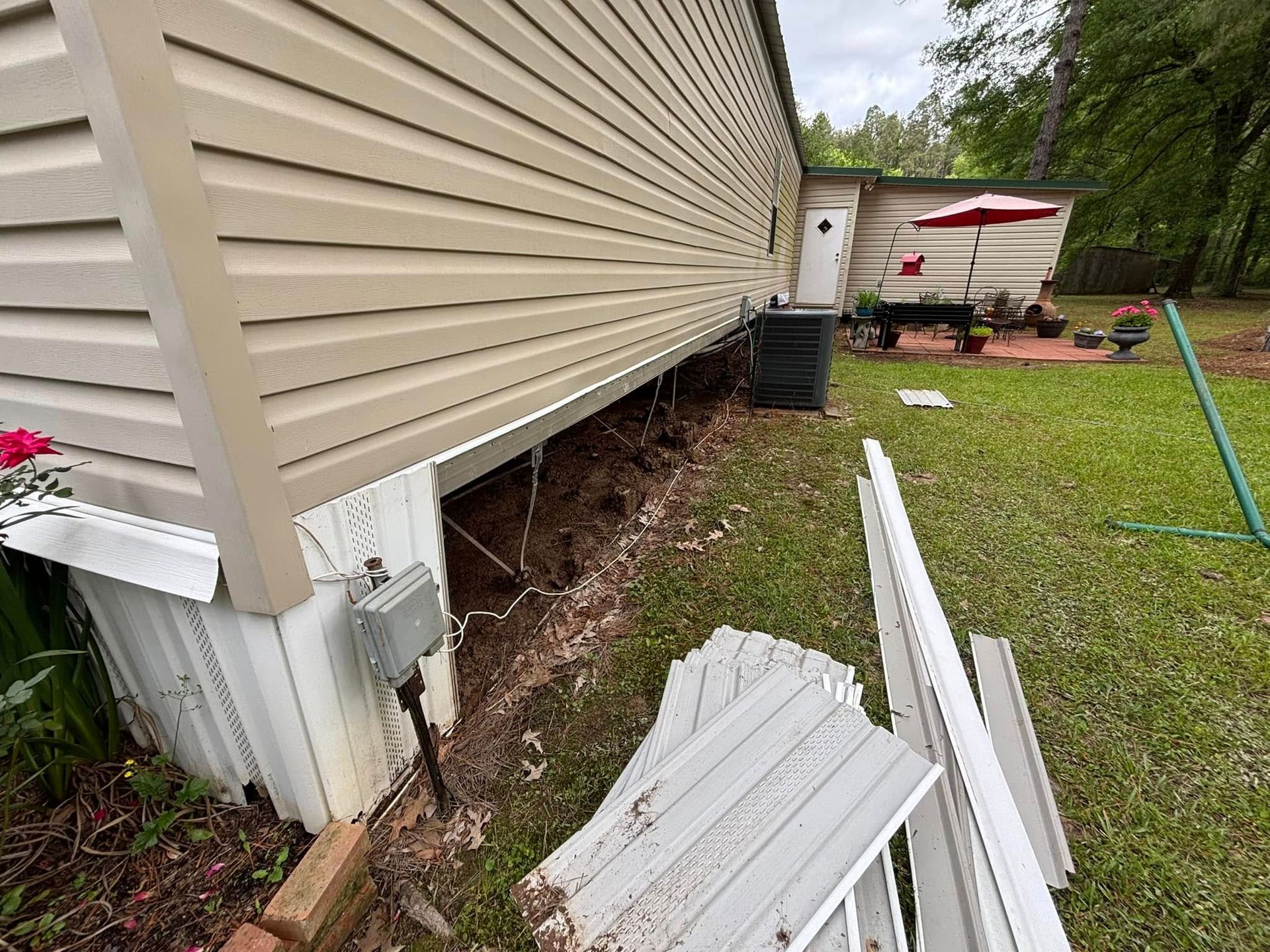 Mobile home exterior with exposed underbelly, beige siding, debris on the ground.
