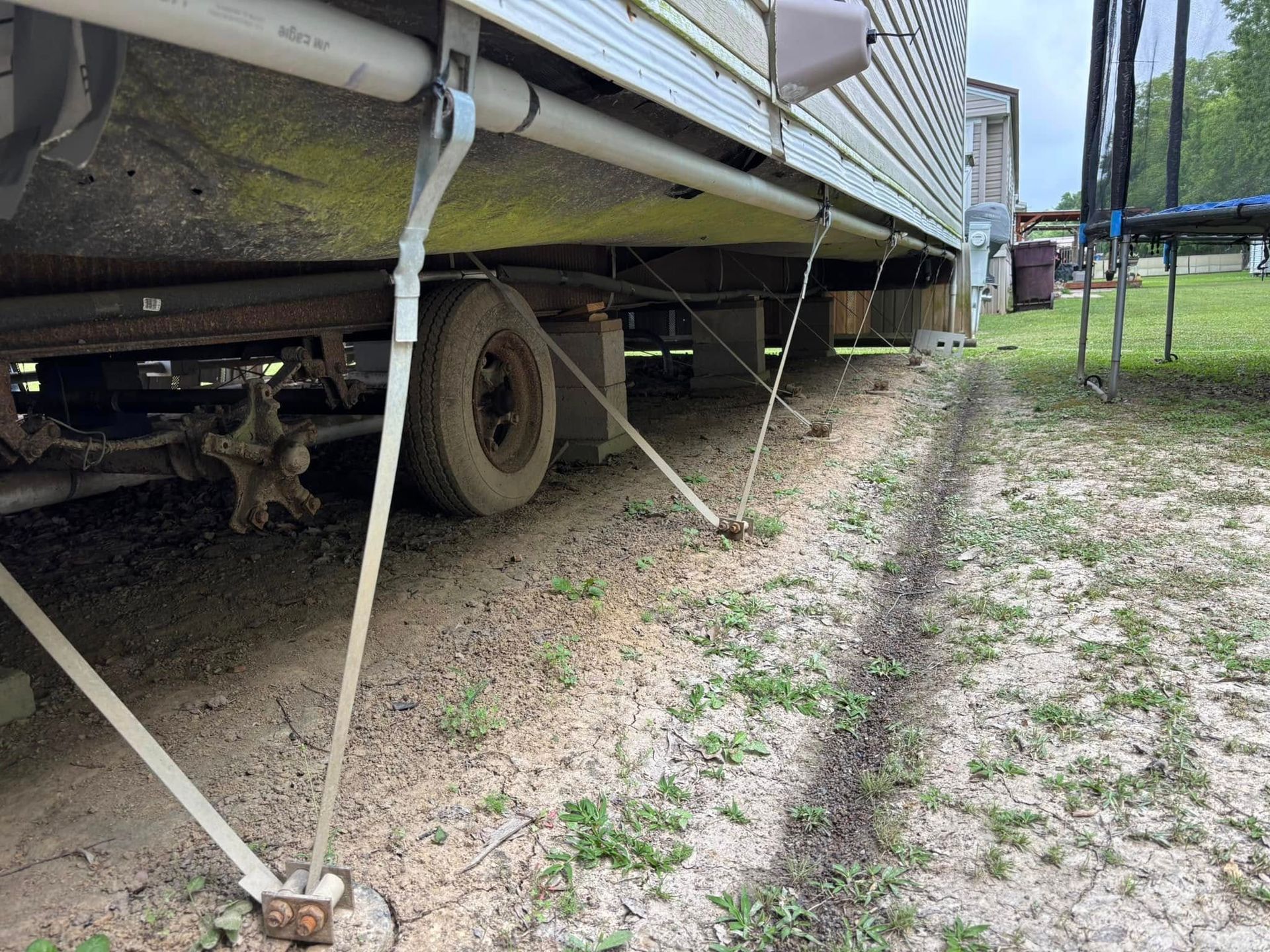 A trailer is sitting on top of a dirt field next to a trampoline.