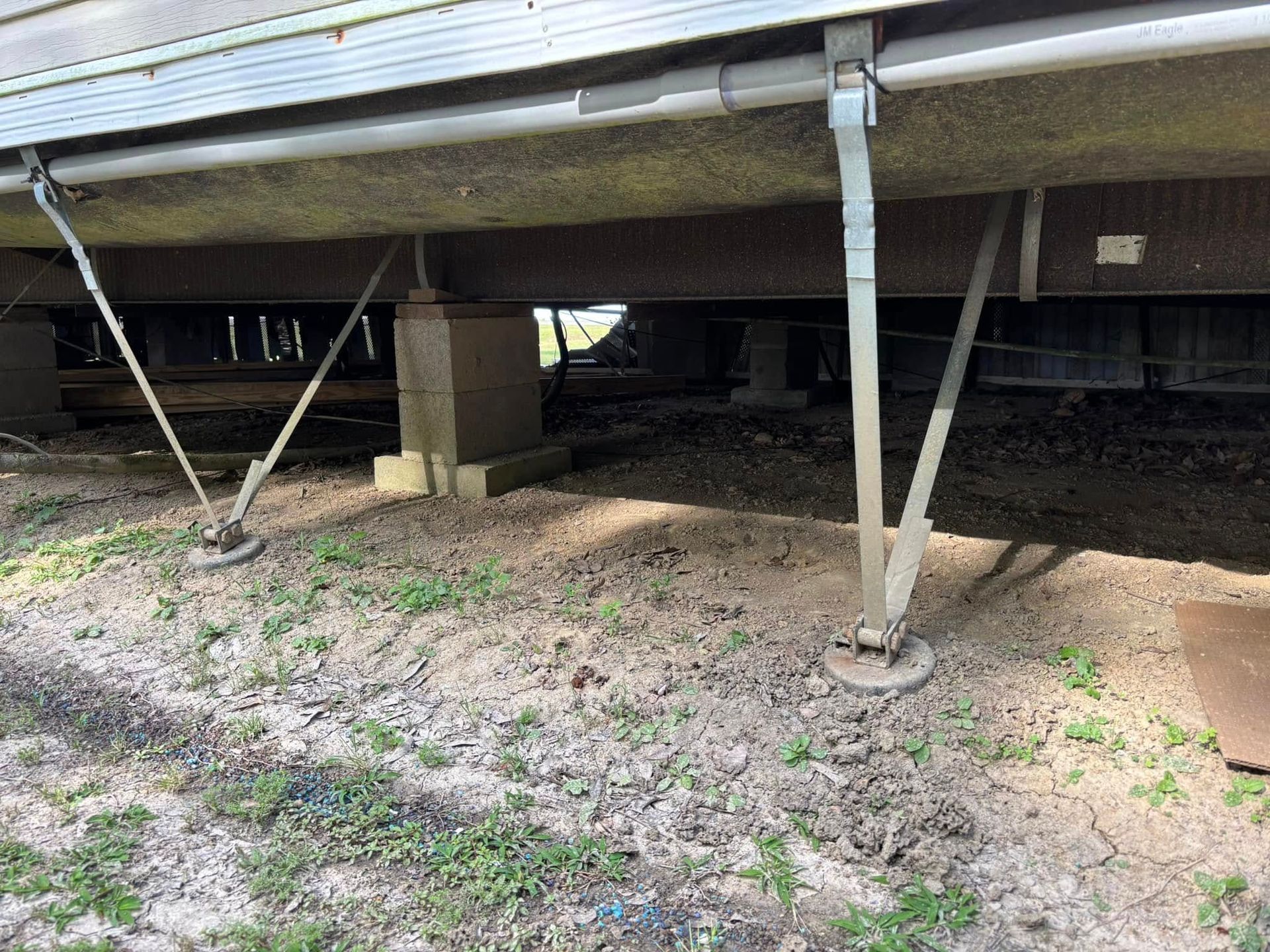 A rv is parked under a house in the dirt.