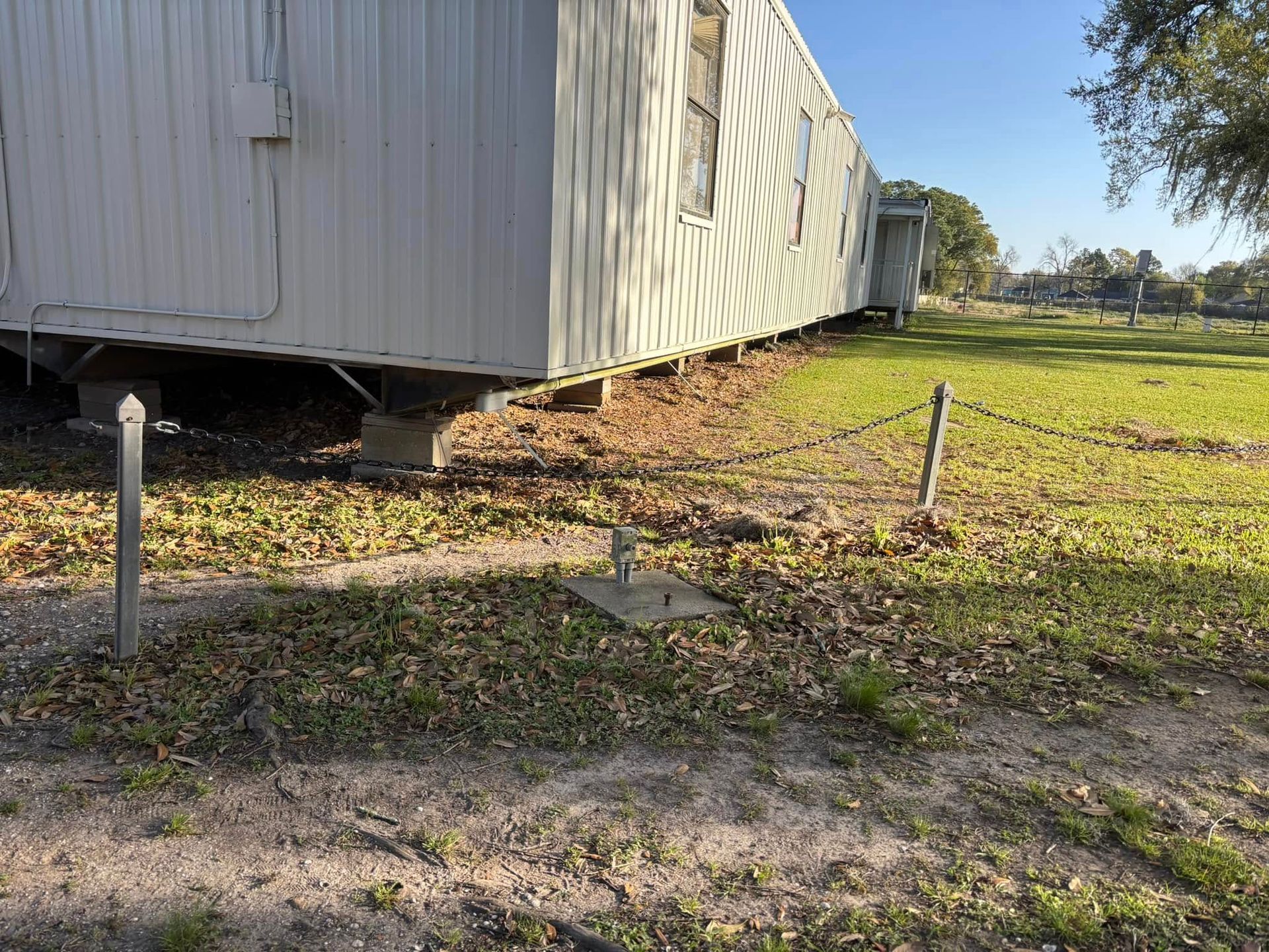 A white trailer is parked in a grassy field next to a chain link fence.