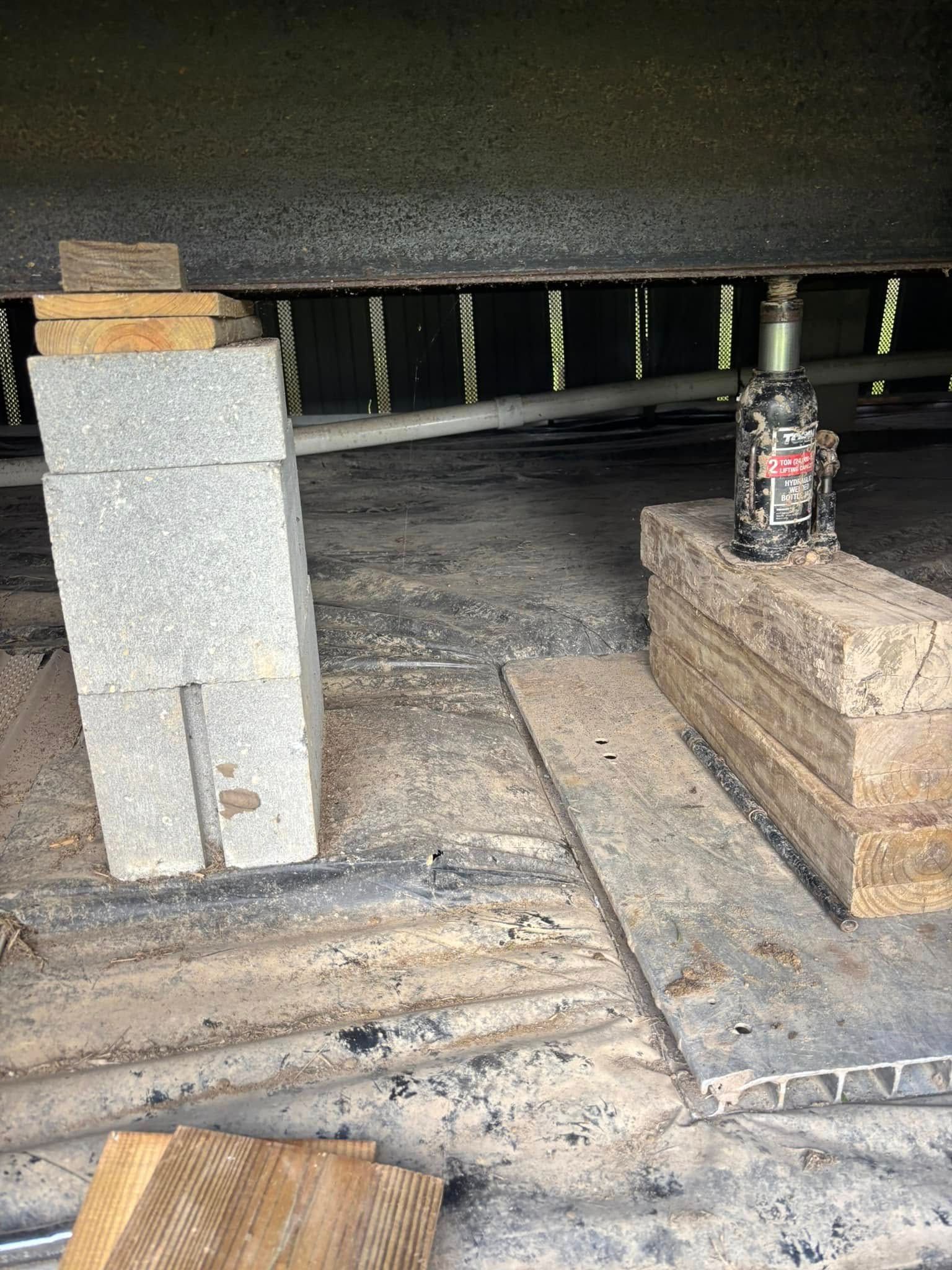 A concrete block is sitting on top of a wooden block next to a jack.