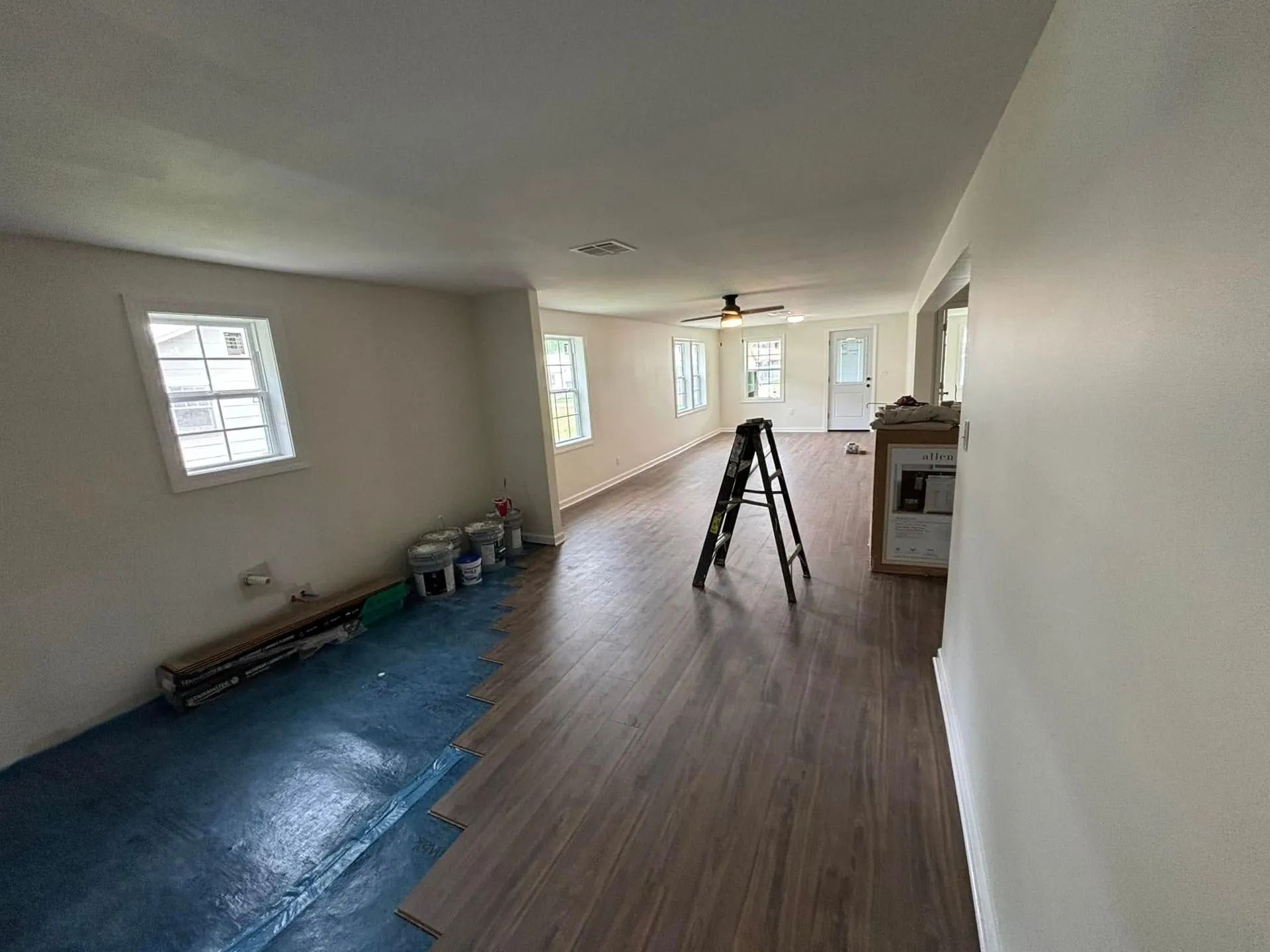 An interior room under renovation with new wood flooring half-installed, a step ladder in the center, and bare walls.