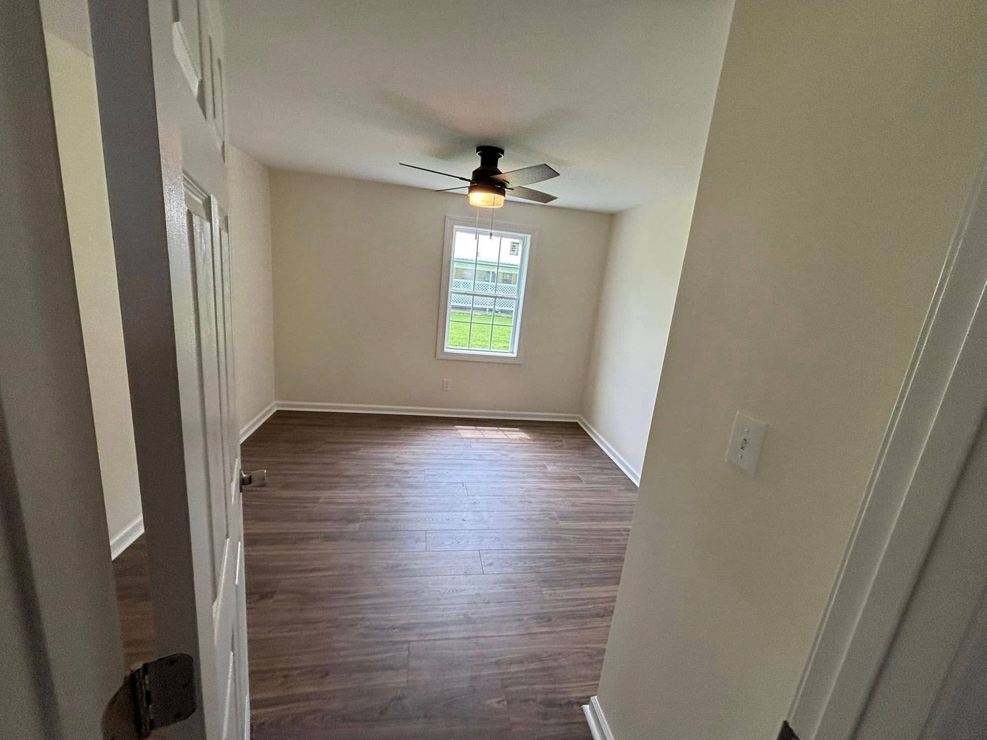 An empty room with a ceiling fan and a window.