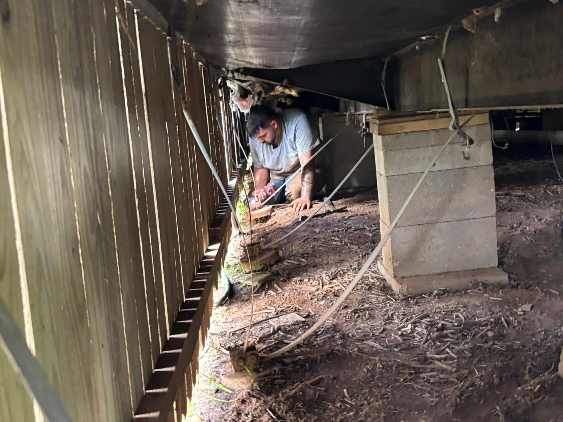 A man is working under a boat in a wooden shed.