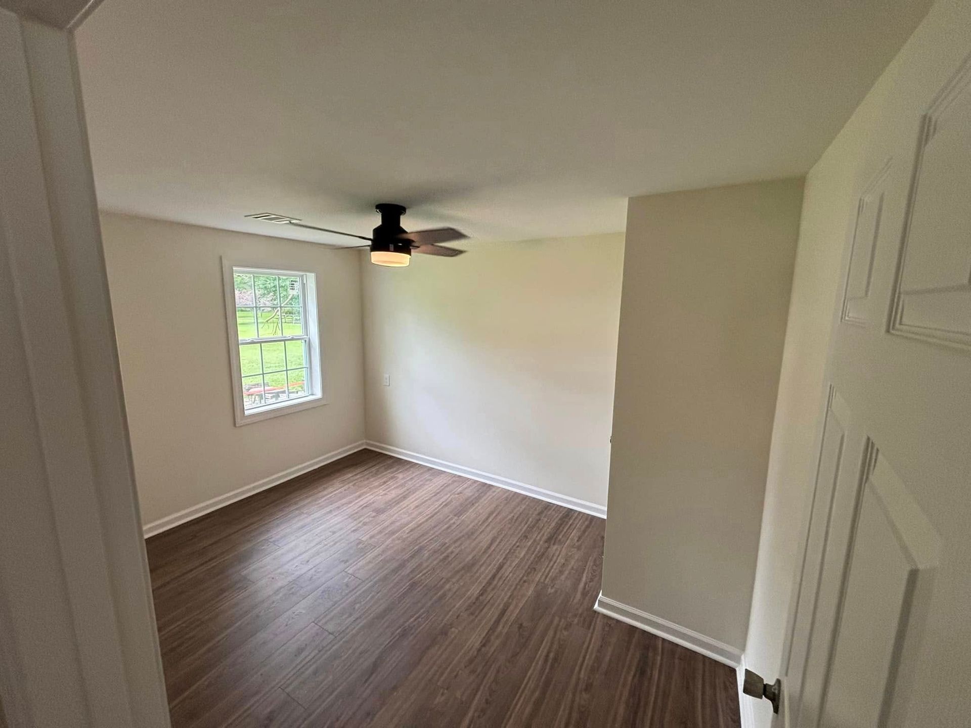 An empty bedroom with a ceiling fan and a window.