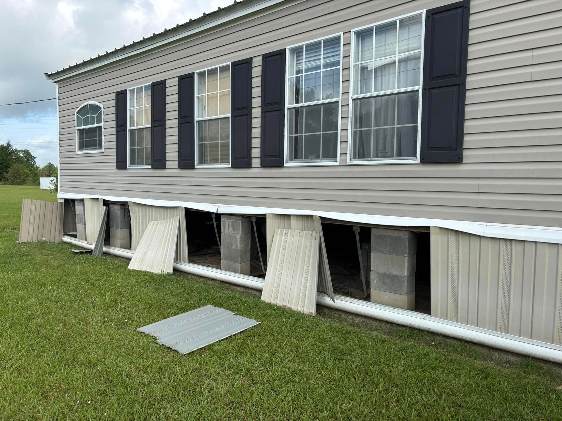 A mobile home with black shutters is sitting on top of a lush green field.