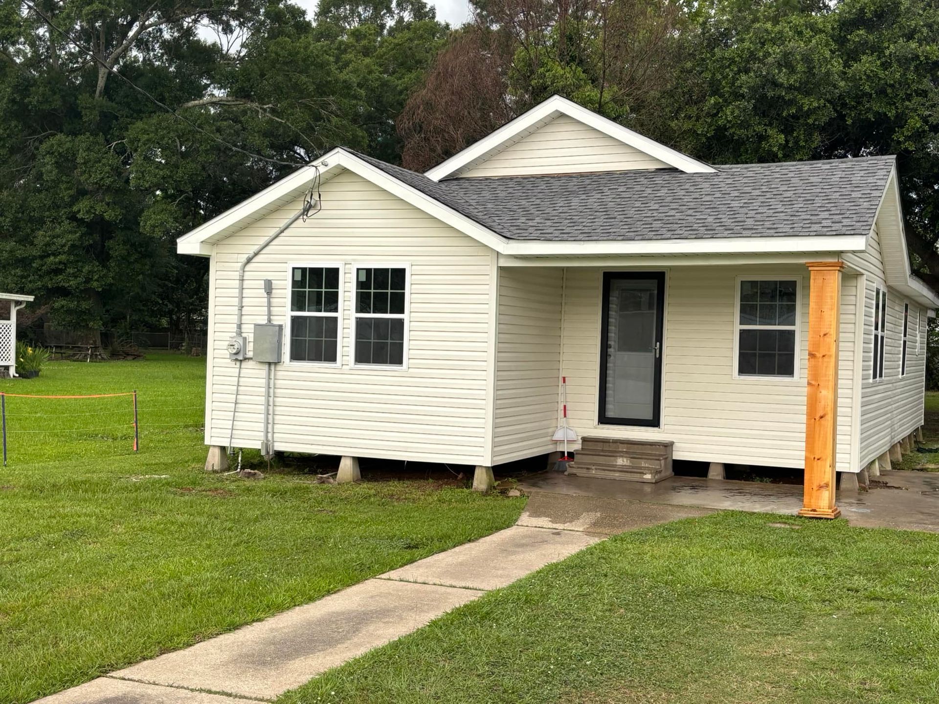Cottage with light siding, dark roof, and small porch on a grassy lawn.