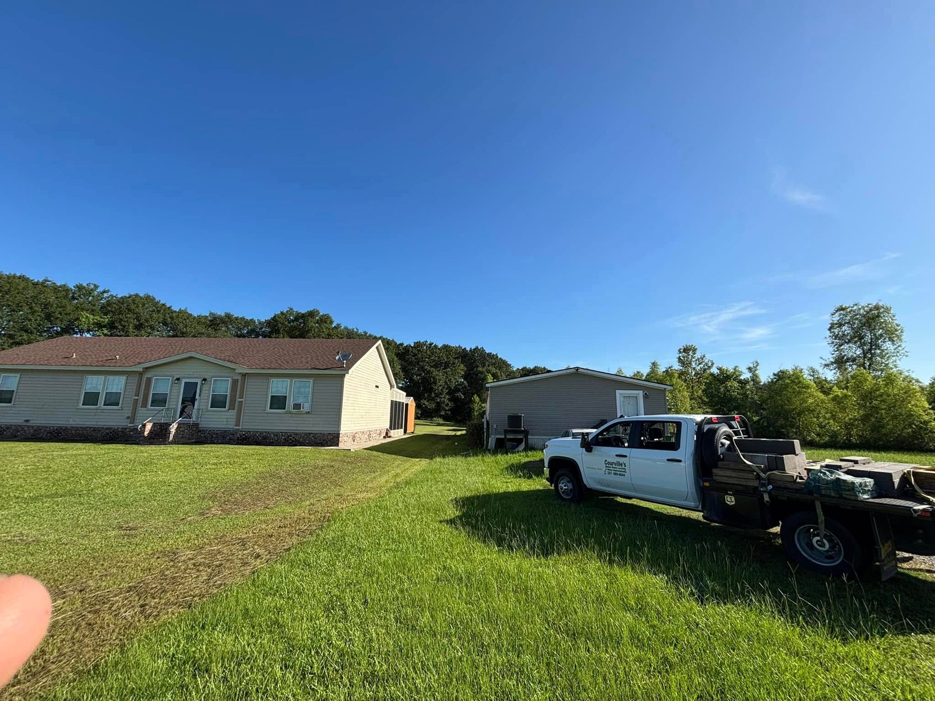 A white truck is parked in a grassy field in front of a house.
