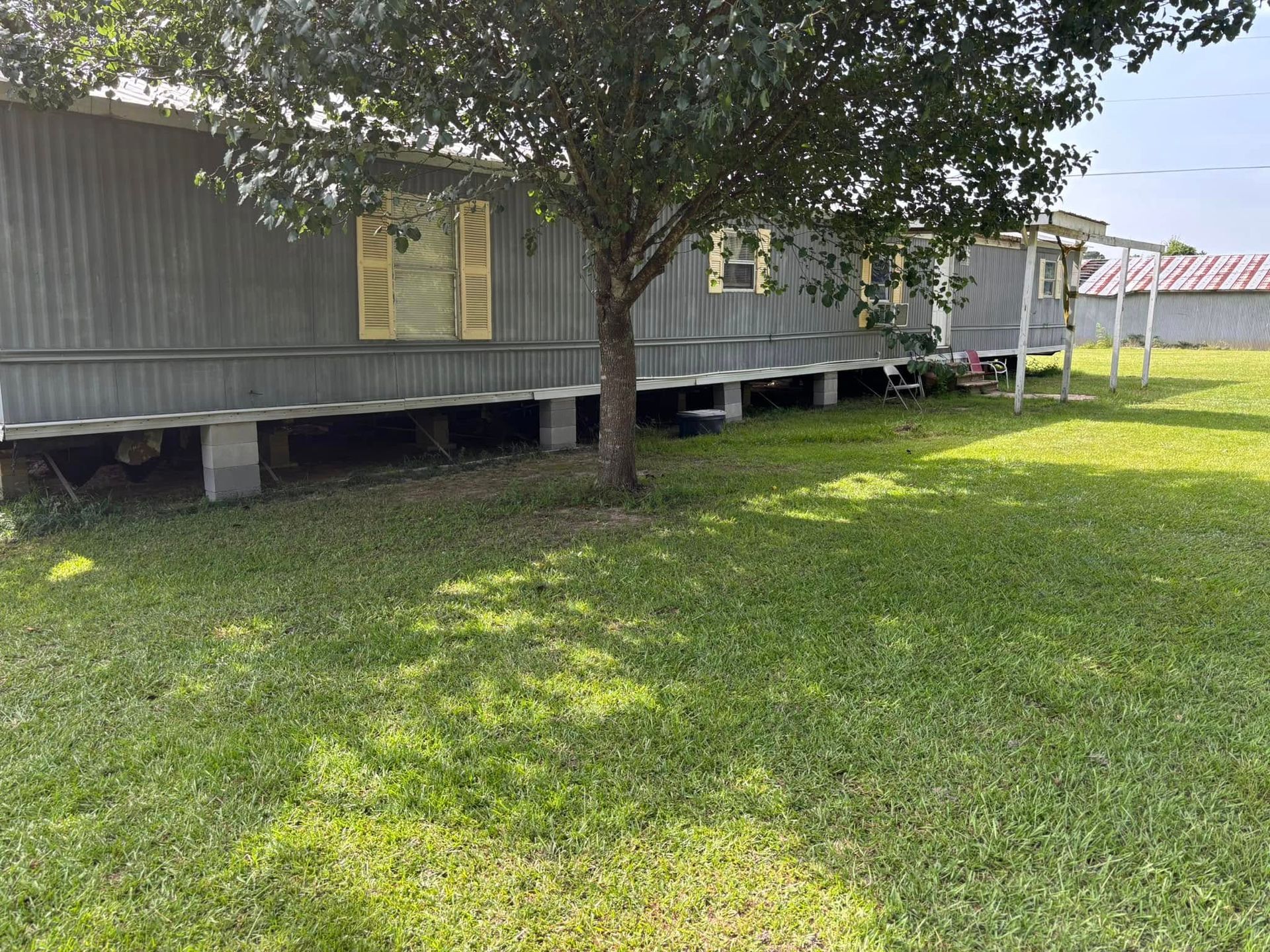 A mobile home is sitting in the middle of a grassy field next to a tree.