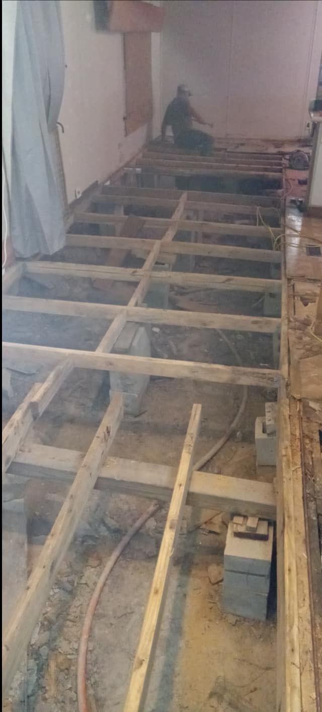 Wooden floor framework construction in progress. Bare joists with a visible worker in the background.