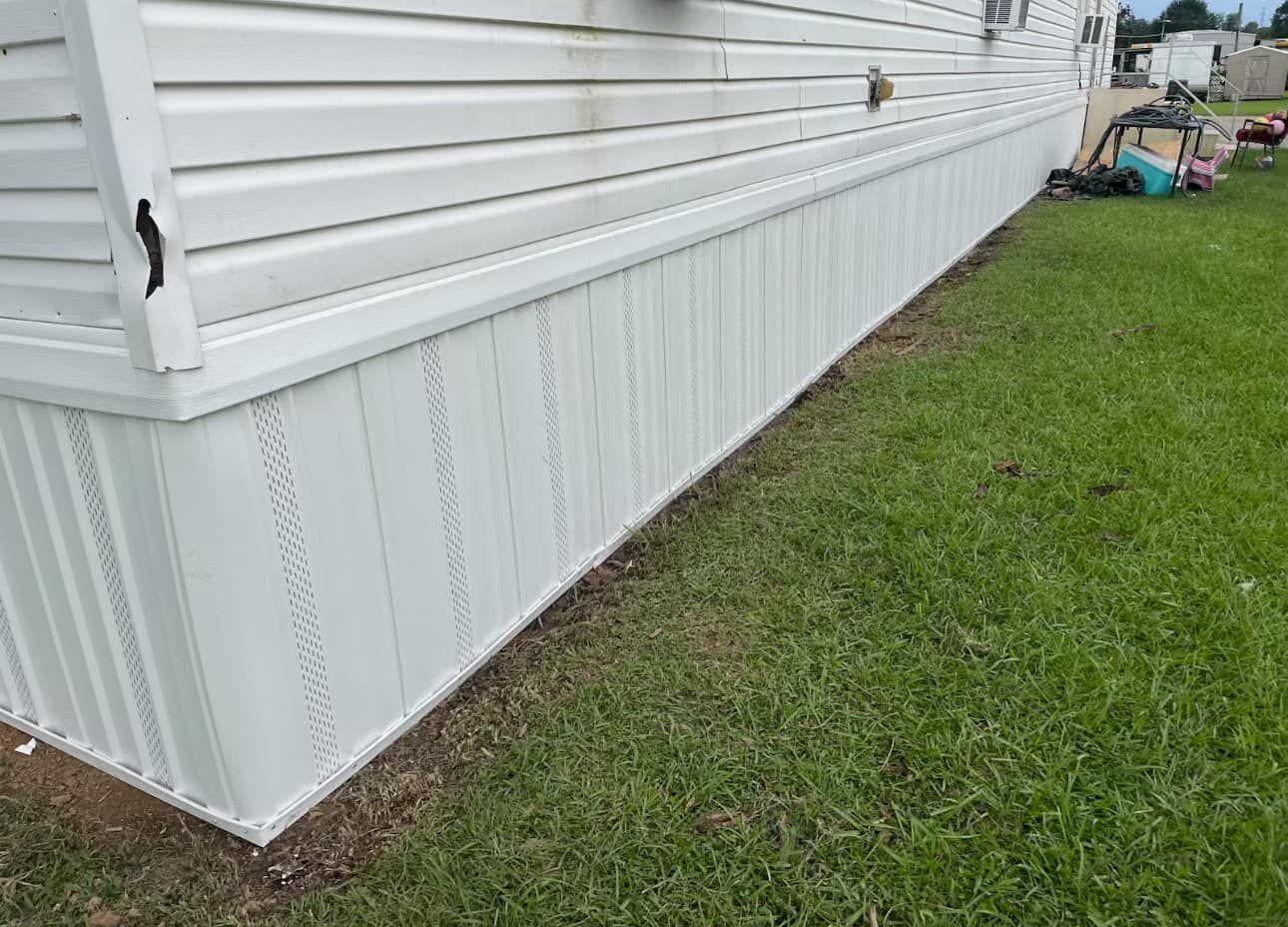 White vinyl skirting of a mobile home on grass.
