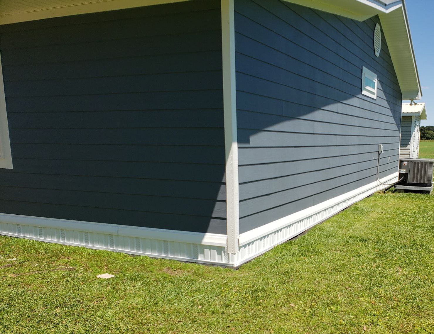 A house with a blue siding and white trim is sitting on top of a lush green field.