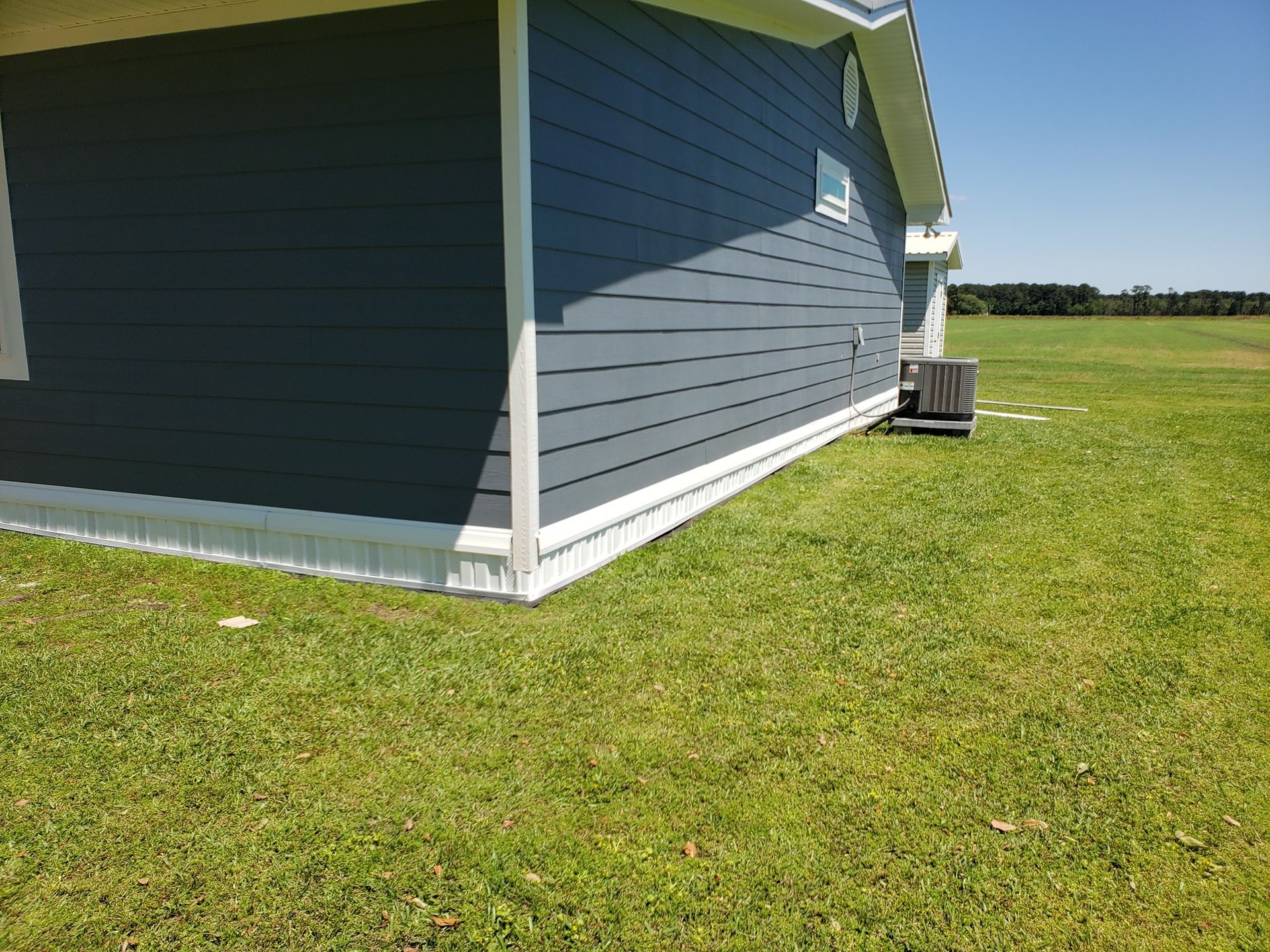 Blue sided house corner with white trim, grassy lawn and blue sky.